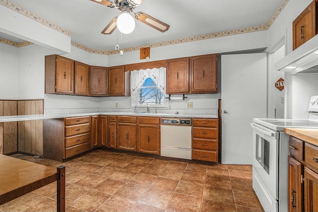 kitchen featuring under cabinet range hood, white appliances, a sink, light countertops, and brown cabinetry