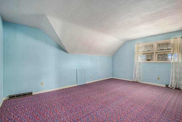 additional living space with a textured ceiling, carpet floors, lofted ceiling, and visible vents