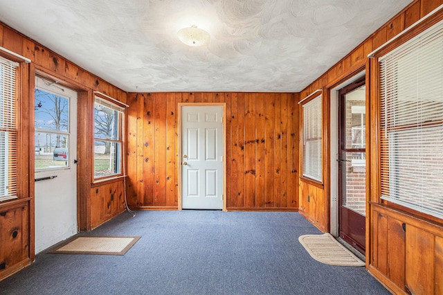 interior space featuring wood walls, a textured ceiling, baseboards, and carpet flooring