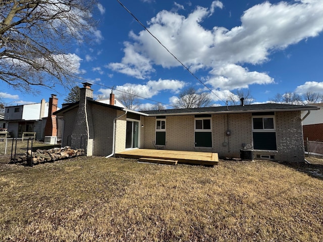 rear view of house featuring a deck, brick siding, fence, a lawn, and a chimney