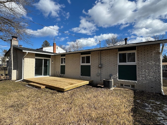 rear view of house featuring a lawn, a chimney, a wooden deck, central air condition unit, and brick siding