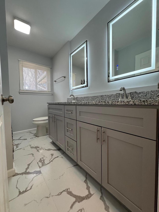 bathroom with marble finish floor, double vanity, a sink, and toilet