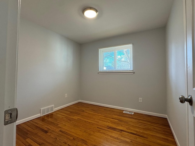 empty room with wood finished floors, visible vents, and baseboards