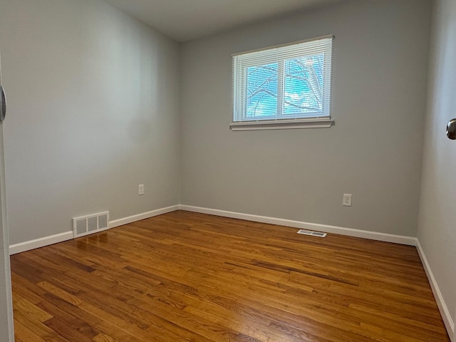 spare room featuring wood finished floors, visible vents, and baseboards