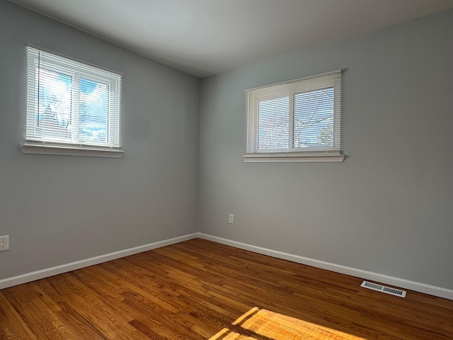 unfurnished room featuring a healthy amount of sunlight, baseboards, visible vents, and wood finished floors