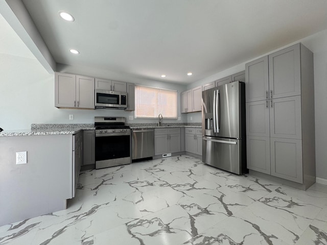 kitchen with light stone countertops, gray cabinets, stainless steel appliances, a sink, and recessed lighting