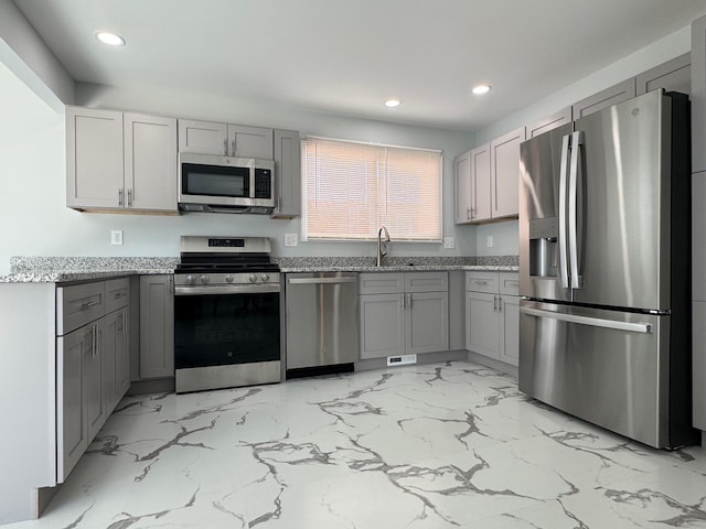 kitchen featuring appliances with stainless steel finishes, light stone counters, a sink, and gray cabinetry