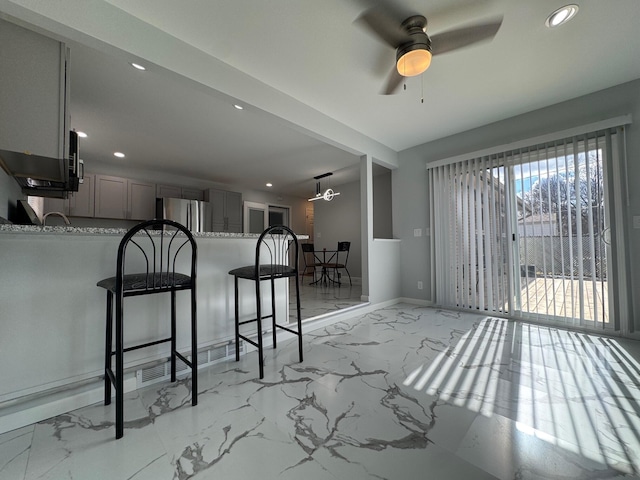 kitchen featuring a breakfast bar, freestanding refrigerator, a peninsula, marble finish floor, and gray cabinets