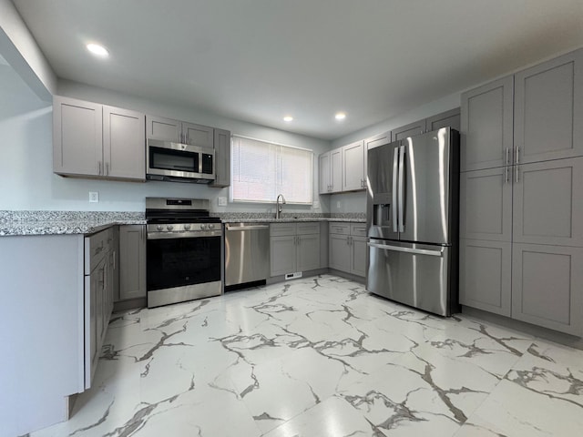 kitchen featuring light stone counters, stainless steel appliances, gray cabinetry, a sink, and recessed lighting