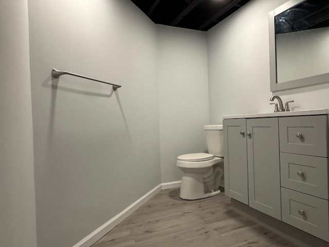 half bath with vanity, wood finished floors, toilet, and baseboards