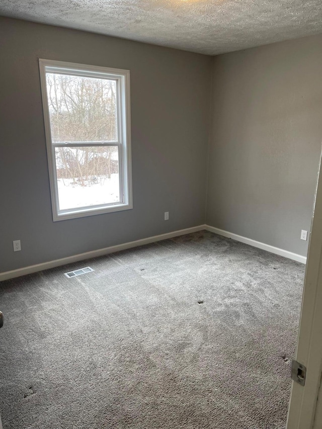 carpeted empty room featuring a textured ceiling, visible vents, and baseboards