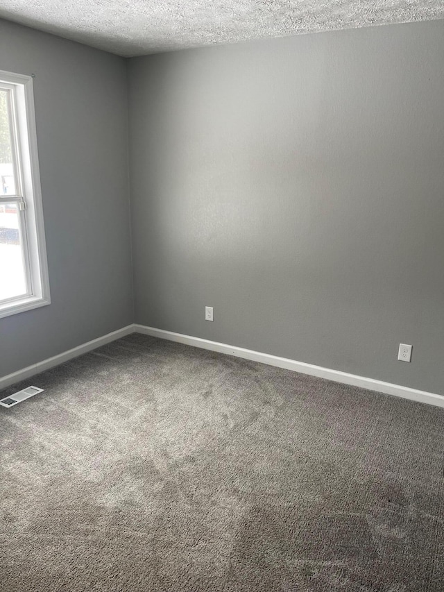 carpeted spare room featuring baseboards, visible vents, and a textured ceiling