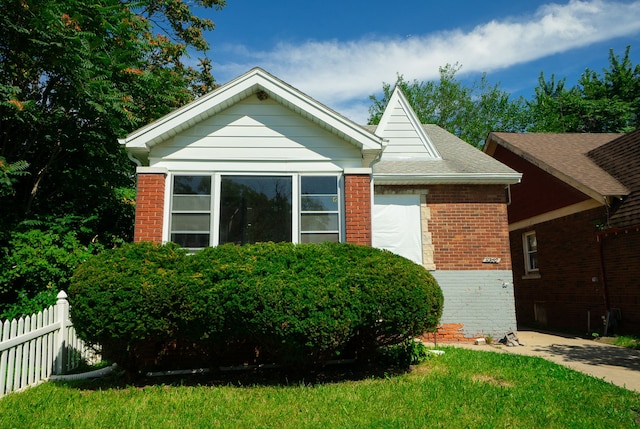 view of front of home featuring brick siding, a front lawn, a shingled roof, and fence