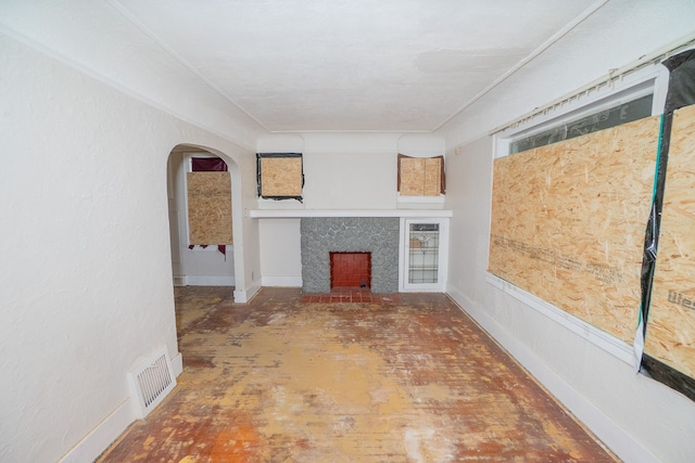 unfurnished living room with arched walkways, a fireplace with raised hearth, visible vents, and baseboards