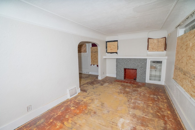 unfurnished living room featuring arched walkways, a premium fireplace, visible vents, and baseboards