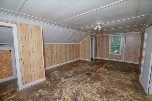additional living space featuring vaulted ceiling, wooden walls, and baseboards