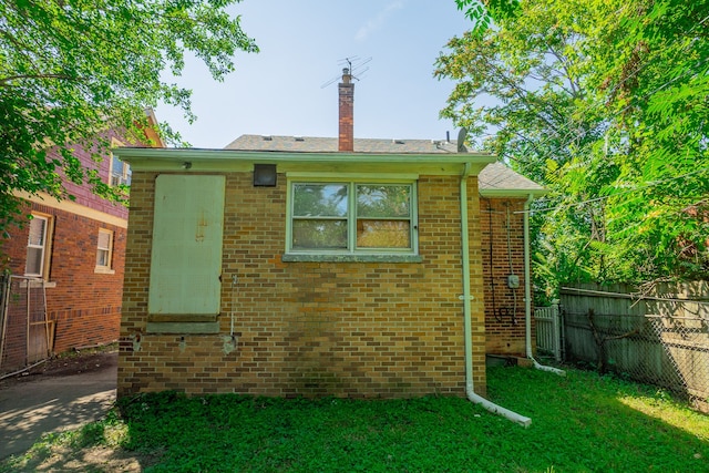 exterior space with brick siding, fence, a chimney, and a lawn
