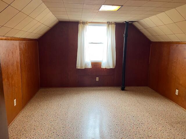 additional living space featuring lofted ceiling and wood walls