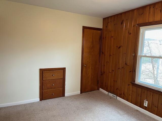 spare room featuring visible vents, wooden walls, baseboards, and carpet flooring