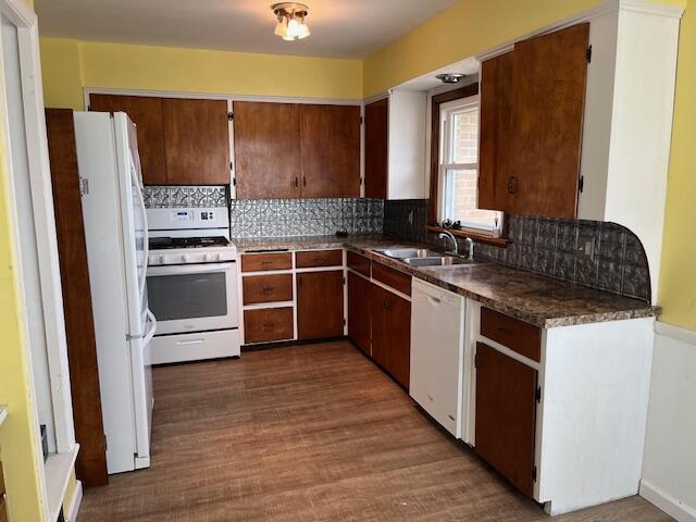 kitchen with white appliances, dark wood finished floors, dark countertops, a sink, and backsplash