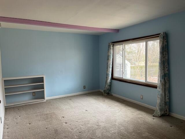 carpeted spare room featuring beam ceiling and baseboards