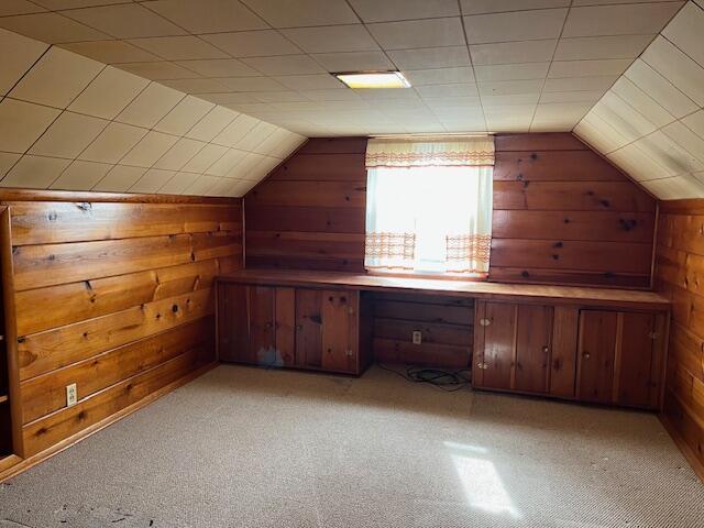 bonus room with lofted ceiling, light colored carpet, and wood walls