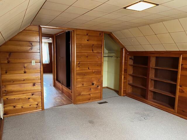 additional living space featuring carpet floors, built in features, lofted ceiling, visible vents, and wood walls