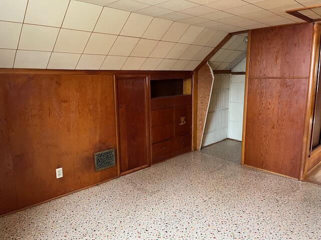 bonus room with vaulted ceiling, wood walls, and visible vents