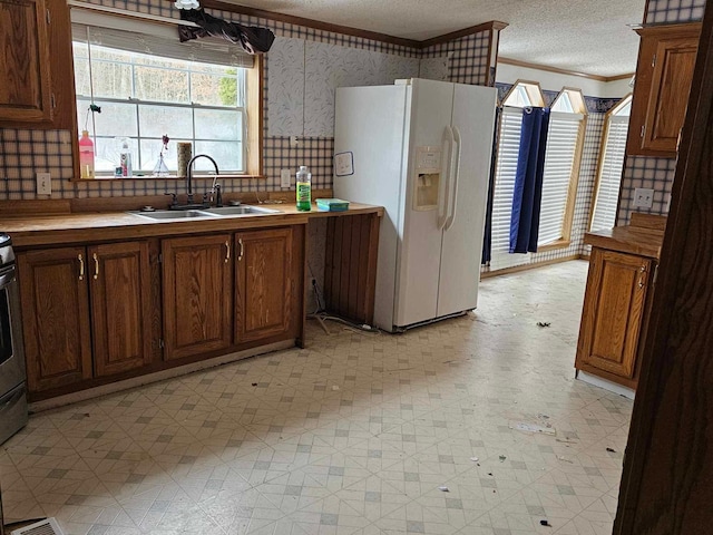 kitchen featuring white refrigerator with ice dispenser, crown molding, a textured ceiling, light floors, and a sink