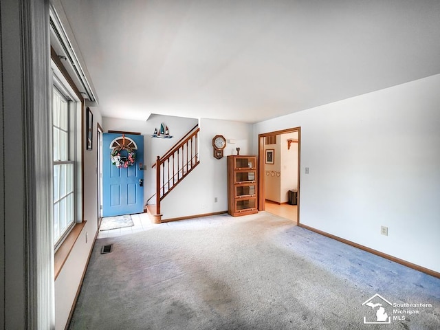 empty room with visible vents, stairway, baseboards, and light colored carpet