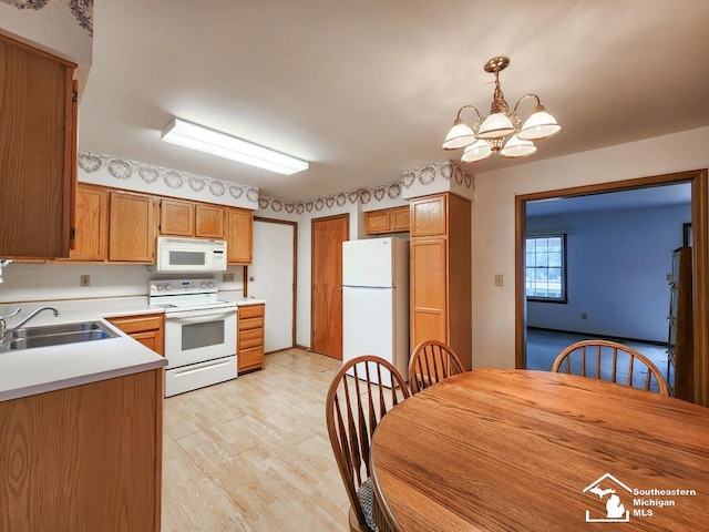 kitchen with a chandelier, white appliances, a sink, light countertops, and light wood-type flooring