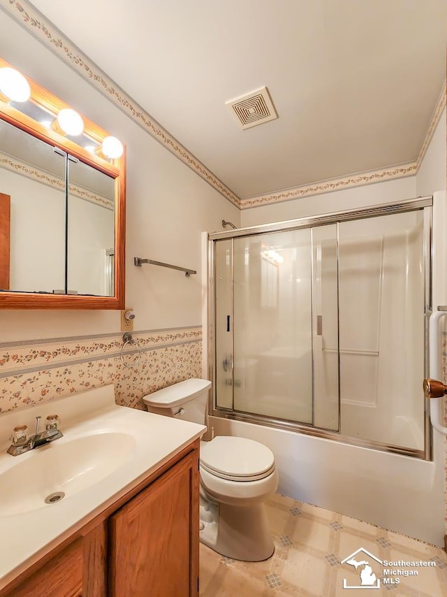 full bathroom with a wainscoted wall, shower / bath combination with glass door, visible vents, toilet, and vanity