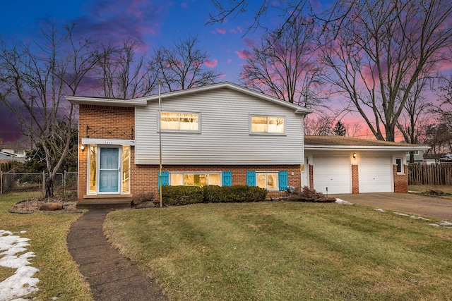 tri-level home with brick siding, concrete driveway, a front yard, fence, and a garage