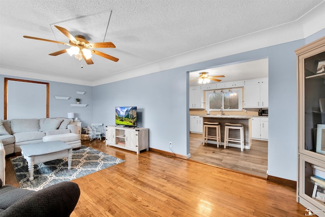 living area featuring light wood-type flooring, ceiling fan, baseboards, and a textured ceiling