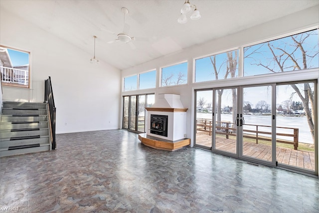 unfurnished living room featuring a healthy amount of sunlight, stairs, high vaulted ceiling, and a glass covered fireplace