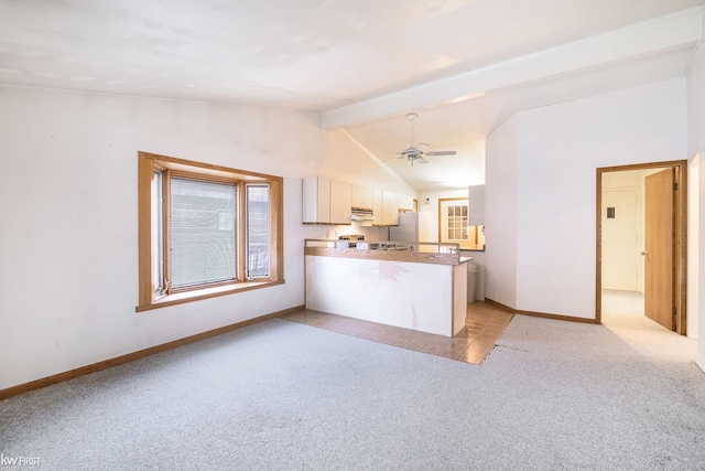 kitchen with vaulted ceiling with beams, light colored carpet, a peninsula, baseboards, and freestanding refrigerator