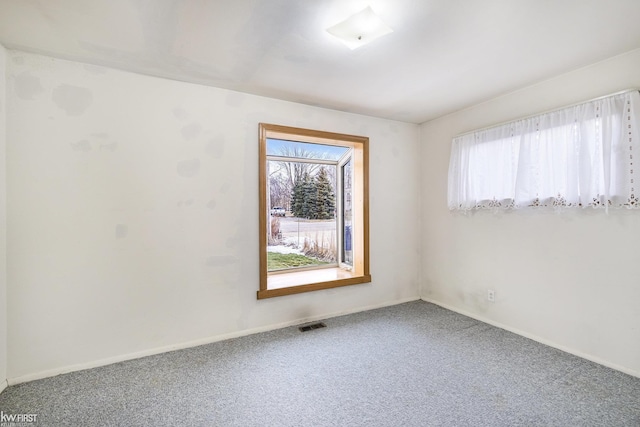 carpeted spare room featuring plenty of natural light, visible vents, and baseboards