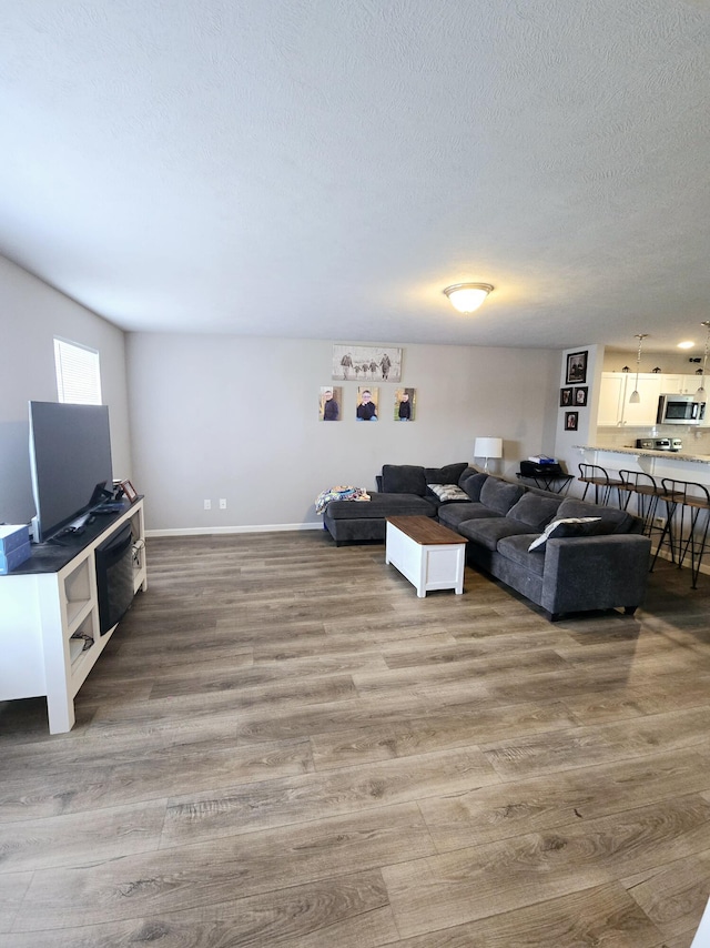 living room featuring a textured ceiling, baseboards, and wood finished floors