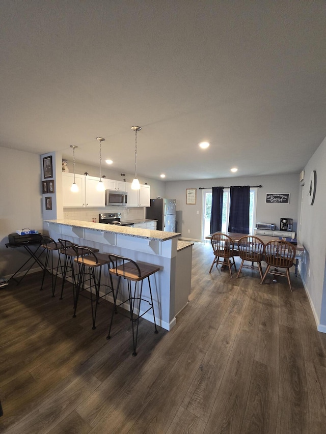 kitchen with a peninsula, a breakfast bar, white cabinets, appliances with stainless steel finishes, and dark wood finished floors