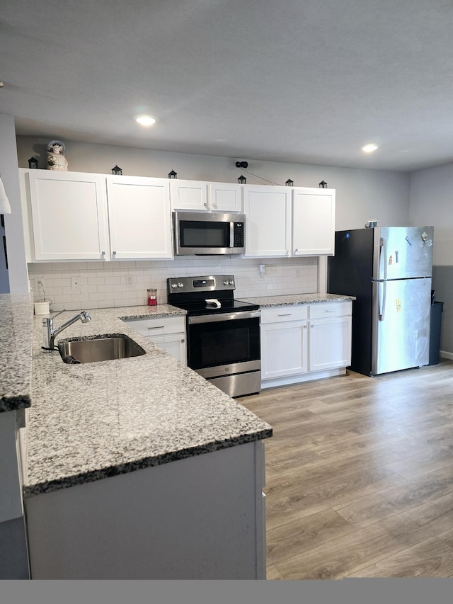 kitchen featuring light stone counters, decorative backsplash, appliances with stainless steel finishes, white cabinetry, and a sink