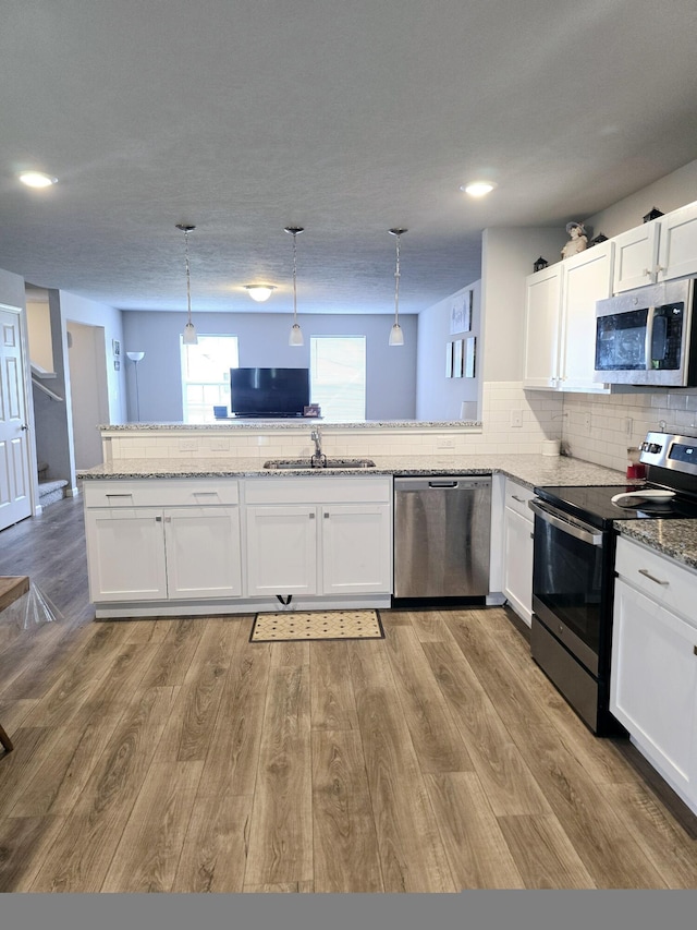 kitchen with stainless steel appliances, white cabinetry, a sink, and light wood finished floors