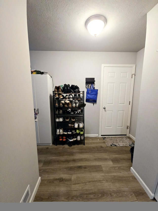 hall featuring a textured ceiling, baseboards, and wood finished floors