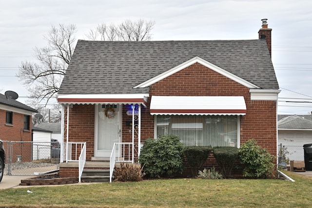 view of front facade with a shingled roof, a chimney, a front lawn, and brick siding