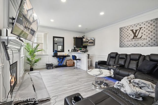 living area featuring crown molding, wood finished floors, a glass covered fireplace, and a decorative wall