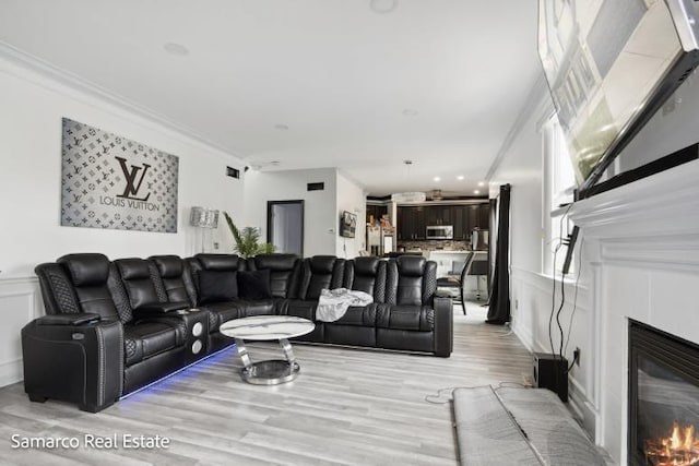 living area featuring ornamental molding, a glass covered fireplace, a decorative wall, and light wood finished floors