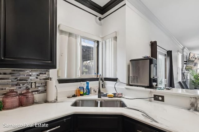 kitchen with crown molding, light countertops, dark cabinetry, and a sink