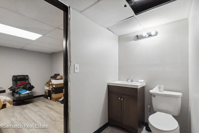 bathroom with a paneled ceiling, toilet, wood finished floors, and vanity