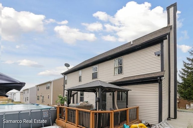 back of house with a wooden deck, an outdoor pool, a chimney, and a gazebo