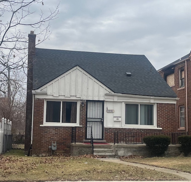 view of front of house with roof with shingles, brick siding, board and batten siding, and fence