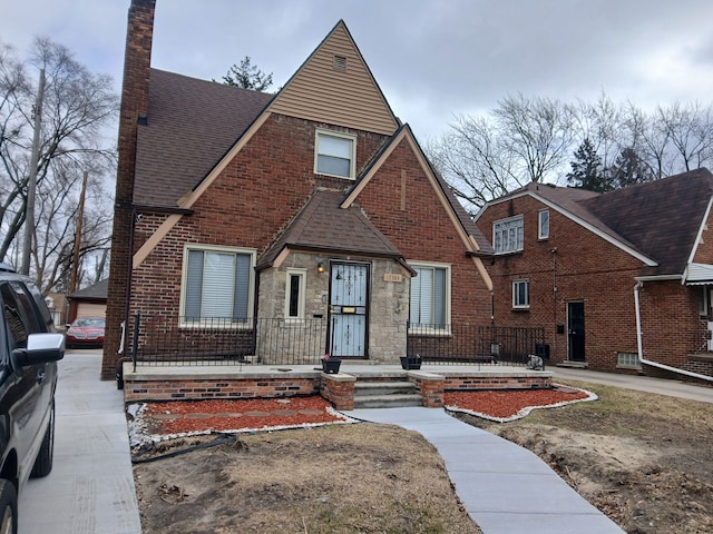 tudor house featuring stone siding, a shingled roof, and brick siding